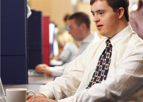 A man with Down syndrome using a computer and drinking coffee